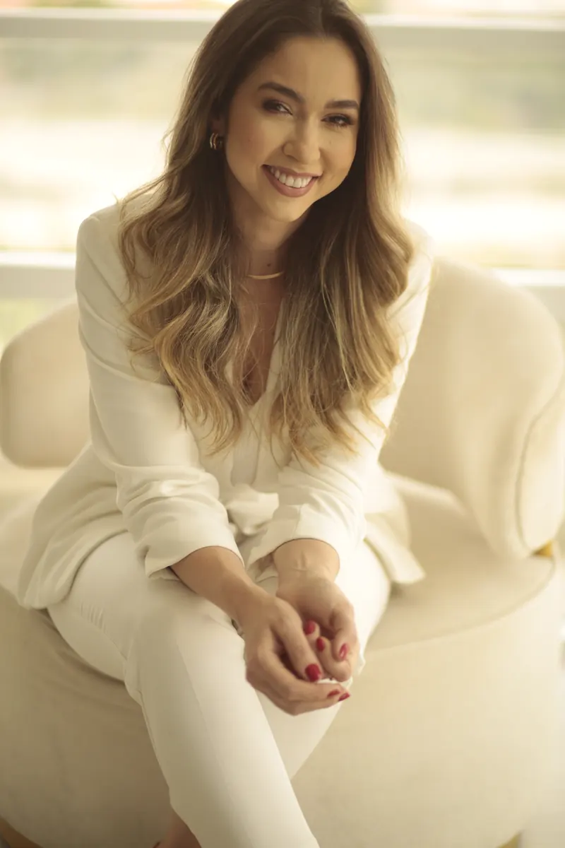 Dra. Fernanda Bardi sentada em uma poltrona, de conjunto creme