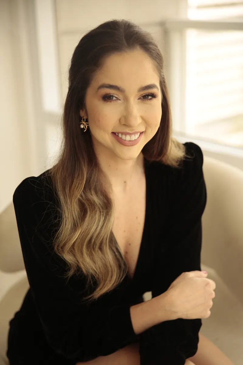 Dra. Fernanda Bardi sentada em poltrona creme, de vestido preto